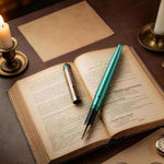 Open book with a teal pen, glasses, and a candle on a wooden surface