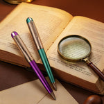 Two pens and a magnifying glass on an open book with a candle in the background